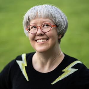 photograph of Laura Langa-Spencer with orange cartoon-style glasses in a black sweater with white and  lime colored lightening bolts on each shoulder aginst a green background